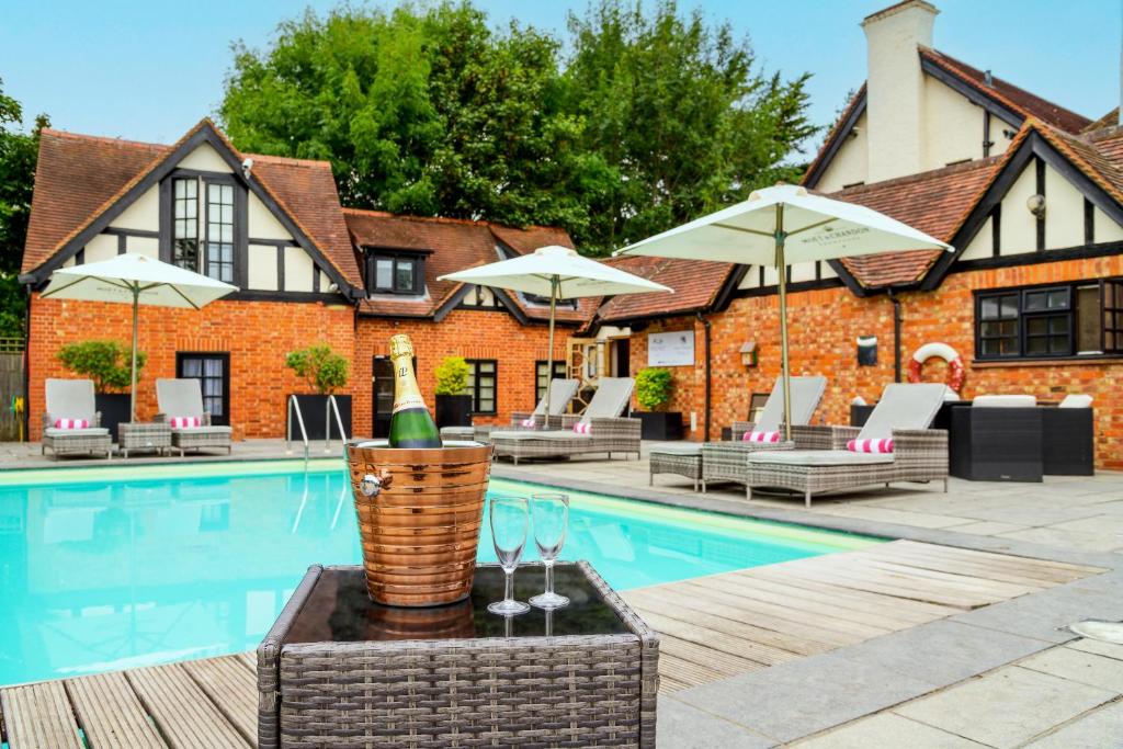 a bottle of champagne and wine glasses next to a swimming pool at Sanctum On The Green Hotel in Cookham Dean