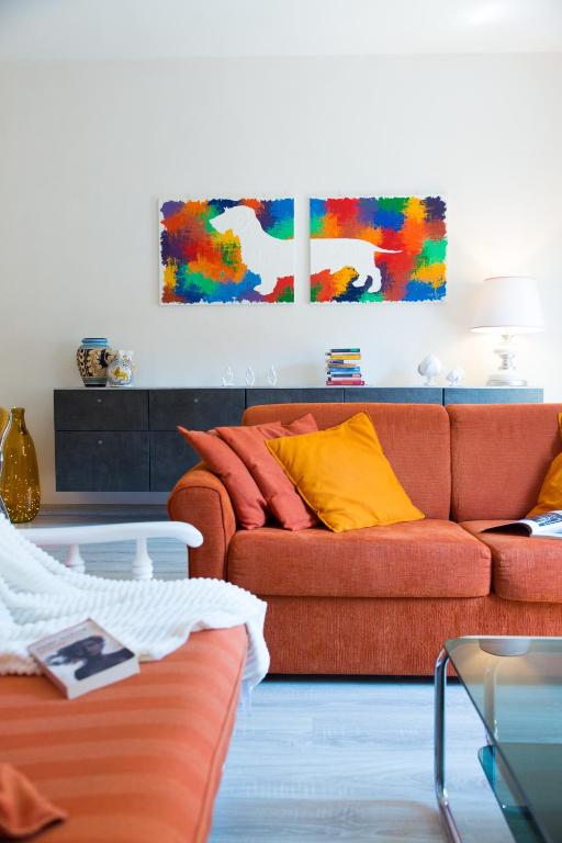a living room with a orange couch and colorful paintings at San Giovanni Apartment in San Gimignano