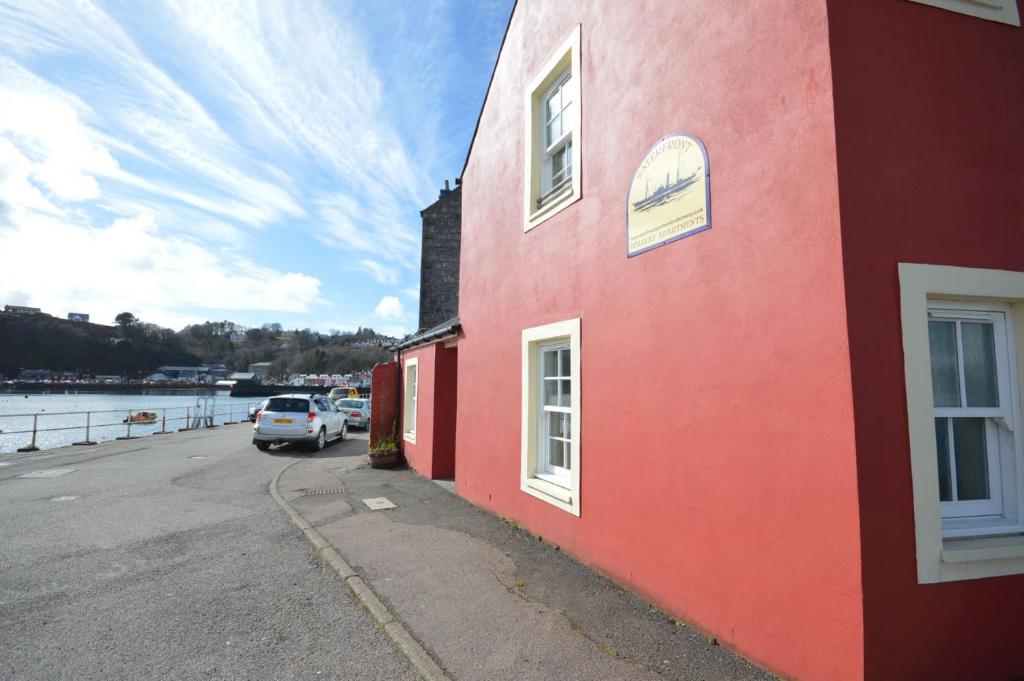 a red building with a car parked next to a body of water at Buzzard Apartment in Tobermory