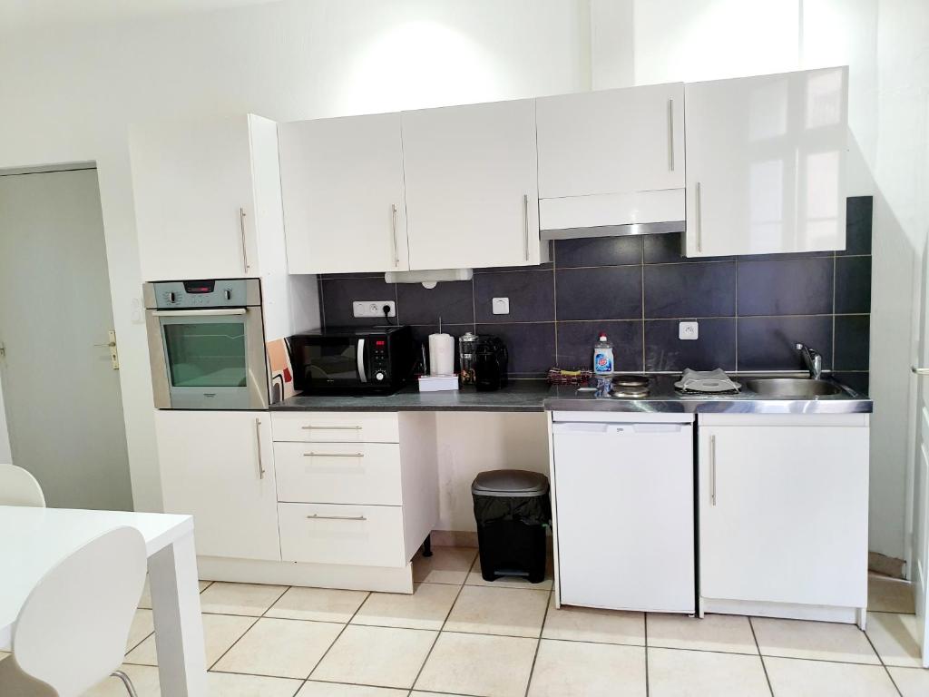 a kitchen with white cabinets and a sink and a microwave at Entre arènes et maison carrée P1 in Nîmes