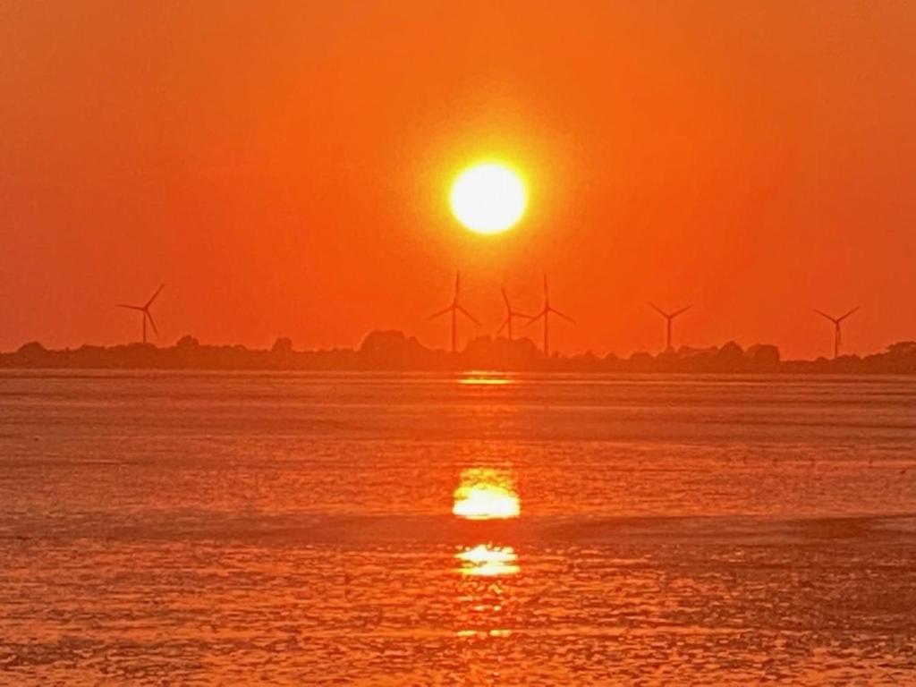 a sunset over the water with windmills in the background at Vier Jahreszeiten in Mildstedt