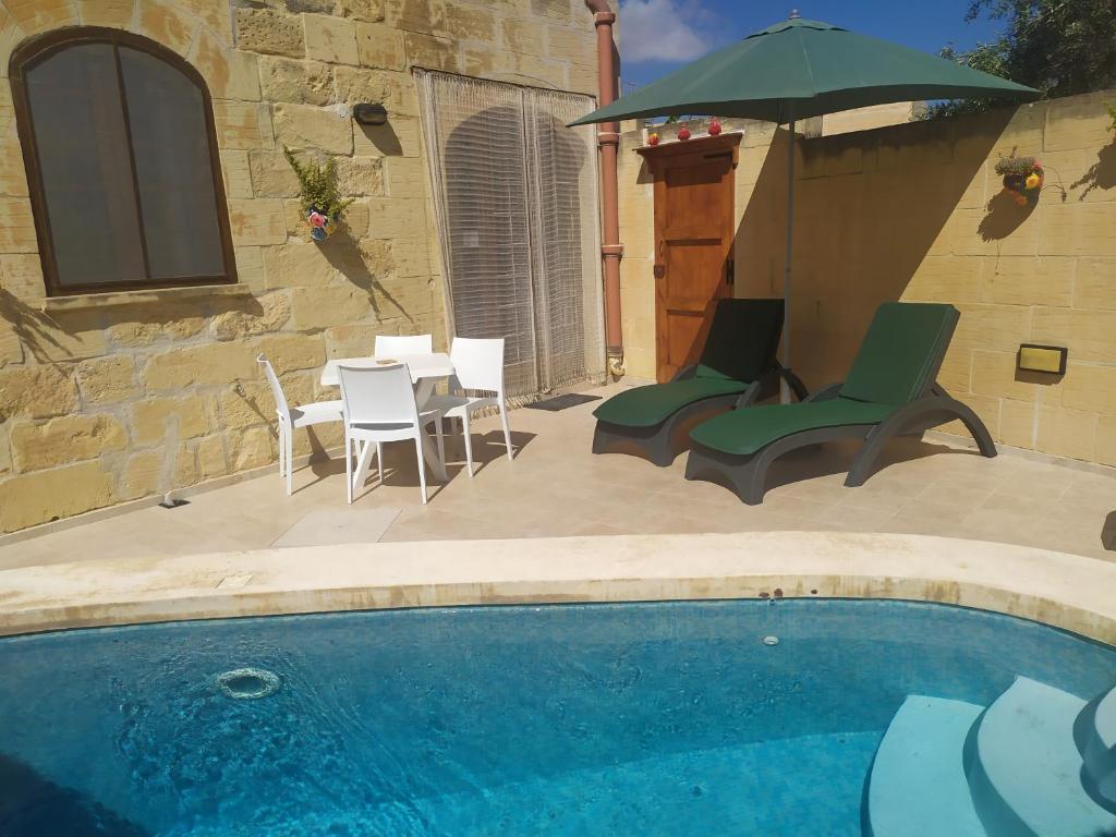 una piscina con sedie, tavolo e ombrellone di Gozo Rustic Farmhouse with stunning views and swimming pool a Sannat