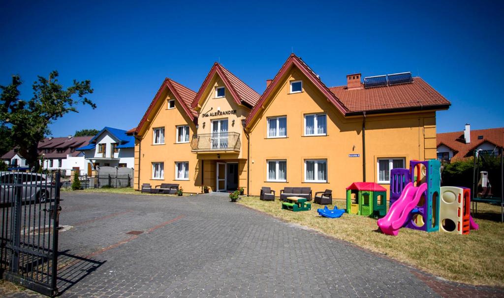 una gran casa amarilla con un parque infantil delante de ella en Willa Aleksander, en Rowy