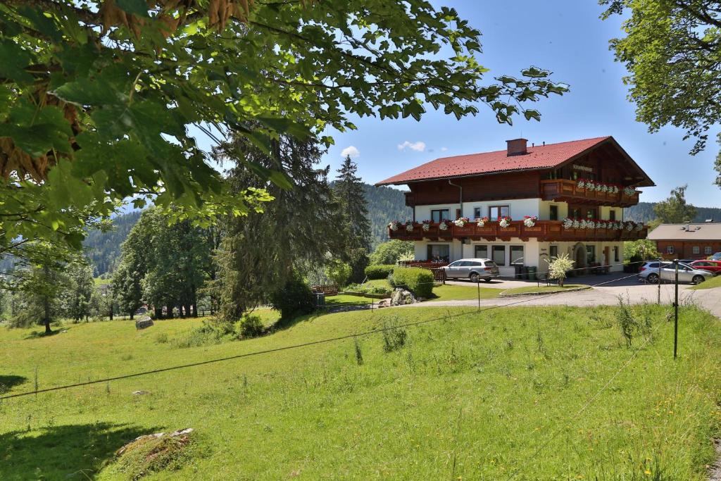 a large house with a red roof on a green field at Pension Sonnwendhof in Ramsau am Dachstein
