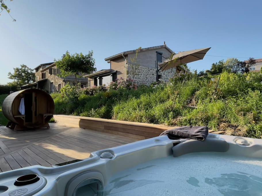 uma banheira num quintal com uma casa ao fundo em Gîte de charme 5 étoiles pour couple avec sauna et jacuzzi extérieurs privatifs em Peaugres