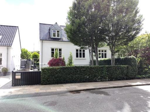 une maison blanche avec une haie en face d'une rue dans l'établissement Værelser i midtbyen - 117 m2 apartment, à Herning