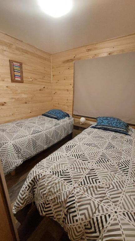 two beds in a room with wooden walls at Cabañas El Roble in Dalcahue