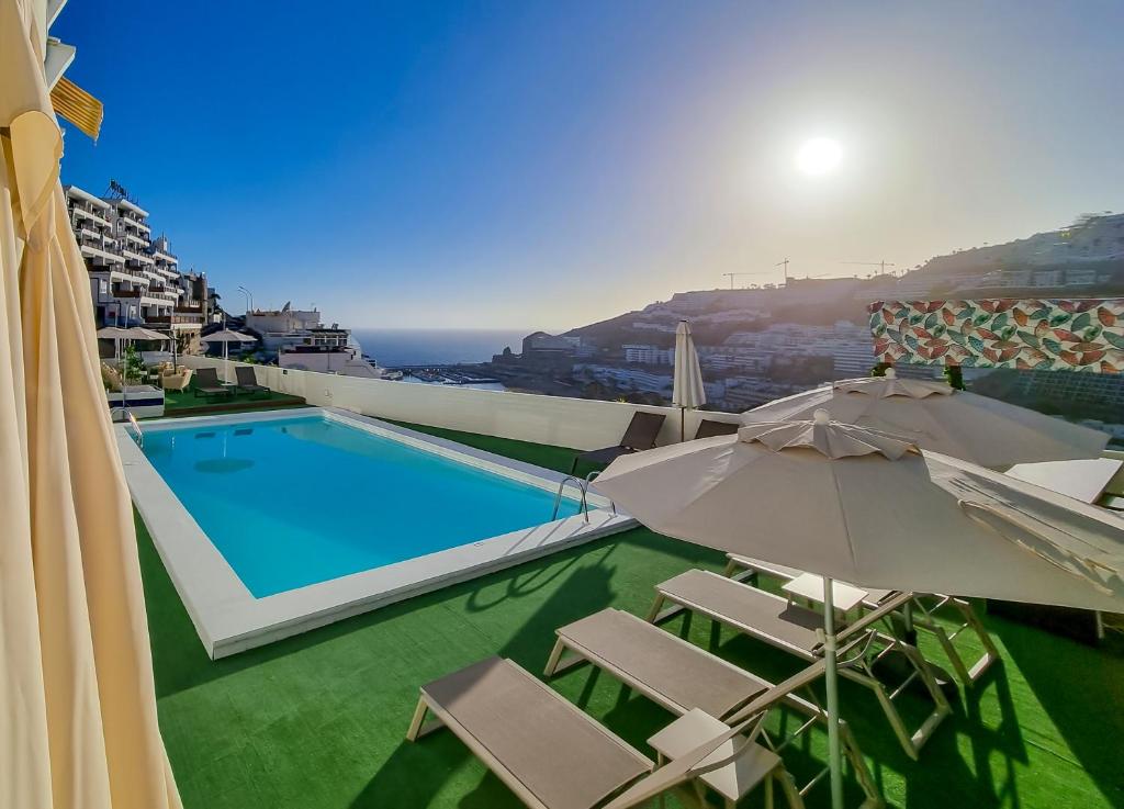 una piscina con sillas y sombrillas en un edificio en Apartamentos Guadalupe Gran Canaria Puerto Rico en Mogán