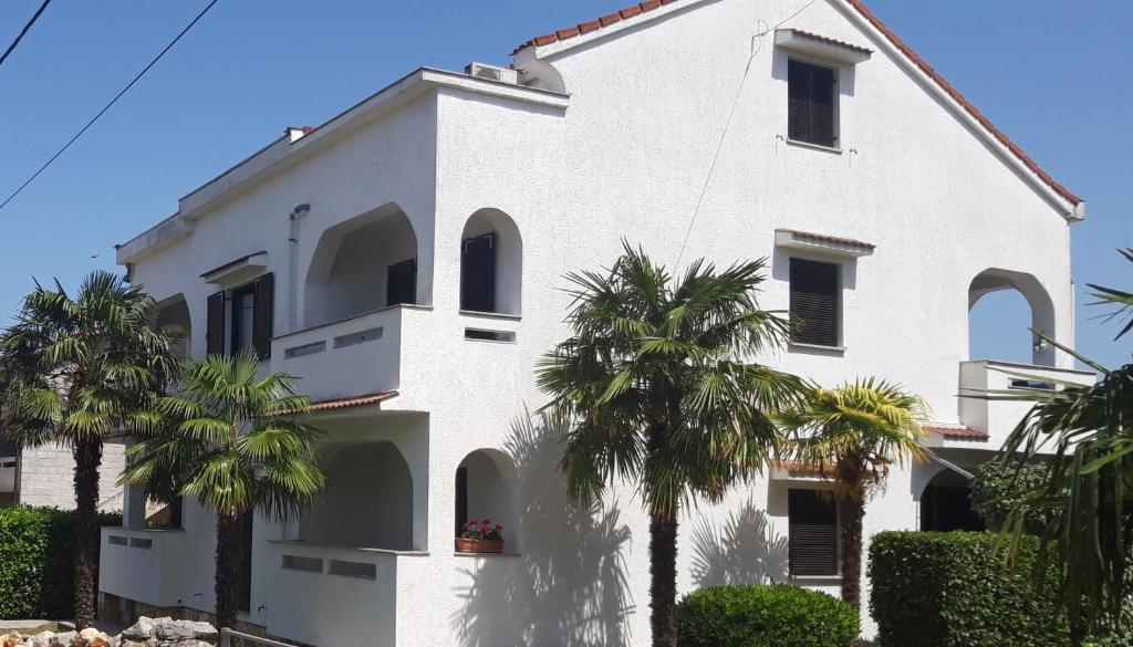 a white building with palm trees in front of it at Apartments with a parking space Sveti Anton, Krk - 5288 in Sveti Anton