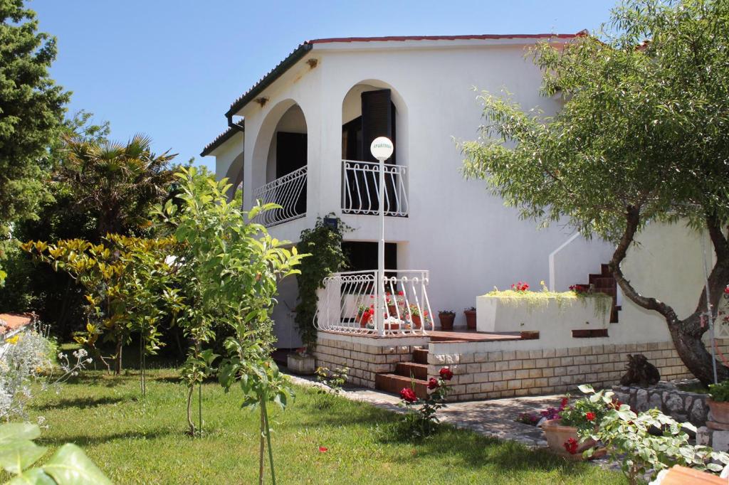 a white house with a porch and a tree at Apartments with a parking space Baska, Krk - 5430 in Baška