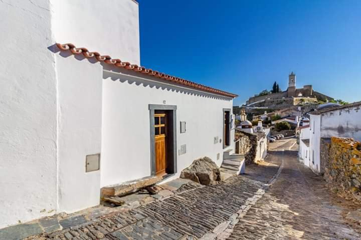 um edifício branco com uma porta castanha numa rua em Casa de São bento - Monsaraz em Monsaraz