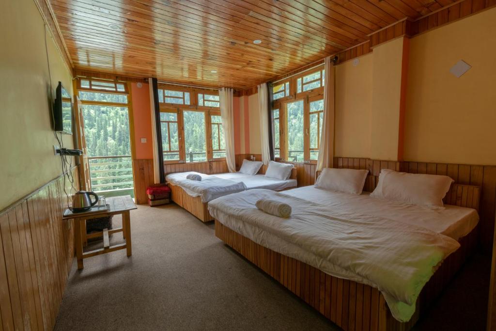 two beds in a room with windows at Venky's Place in Jibhi