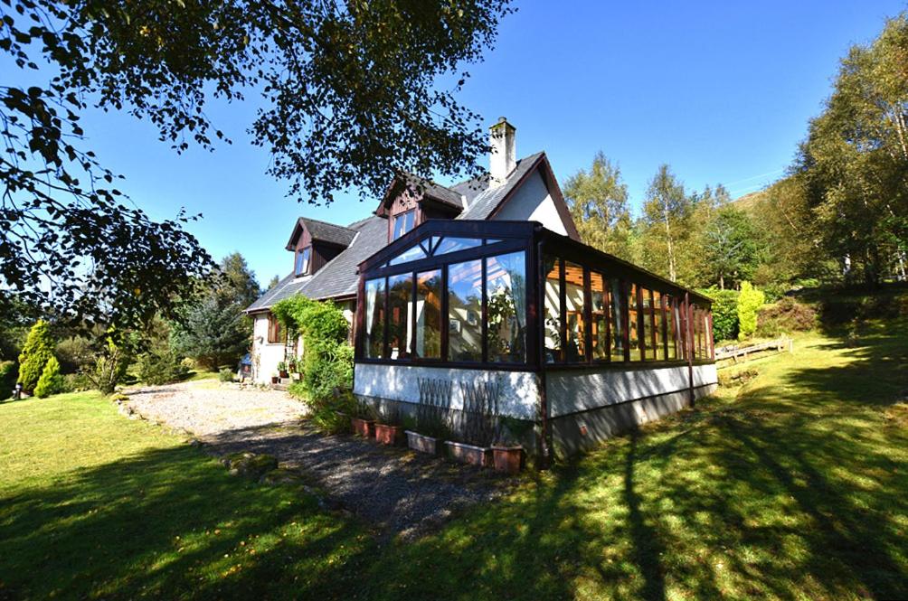 uma casa com muitas janelas num quintal em Tarmachan Cottage - West Highland Getaway em Fort William