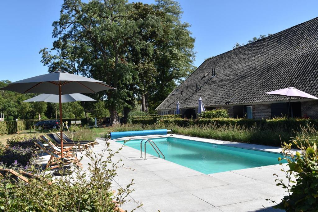 uma piscina com um guarda-sol e uma casa em De Kasteelboerderij em Ruurlo