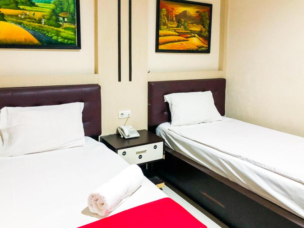 Cette chambre comprend deux lits et un téléphone sur une table. dans l'établissement RedDoorz @ Jalan Arifin Ahmad Pekanbaru, à Parit
