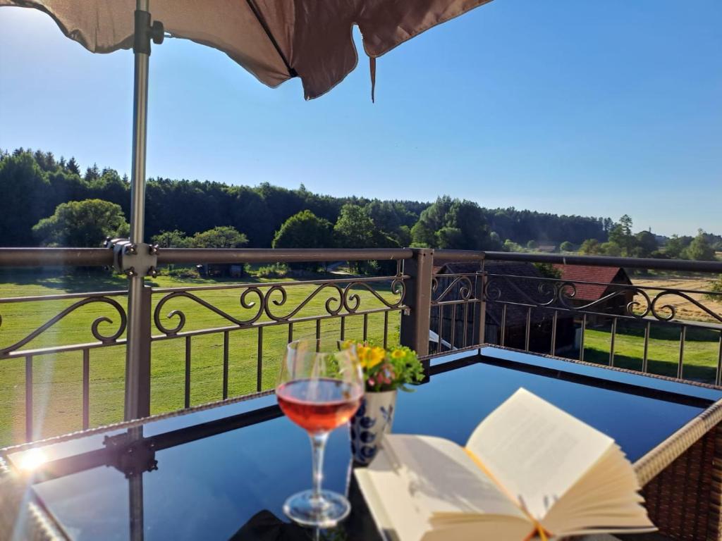 a table with a glass of wine and a book on a balcony at Nuibauers-Hof in Erlenmoos