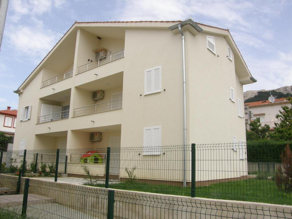 un bâtiment blanc avec une clôture devant lui dans l'établissement Apartment Pavlakovic, à Baška