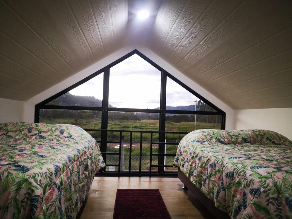 2 Betten in einem Zimmer mit einem großen Fenster in der Unterkunft Cabañas Killari in Oxapampa
