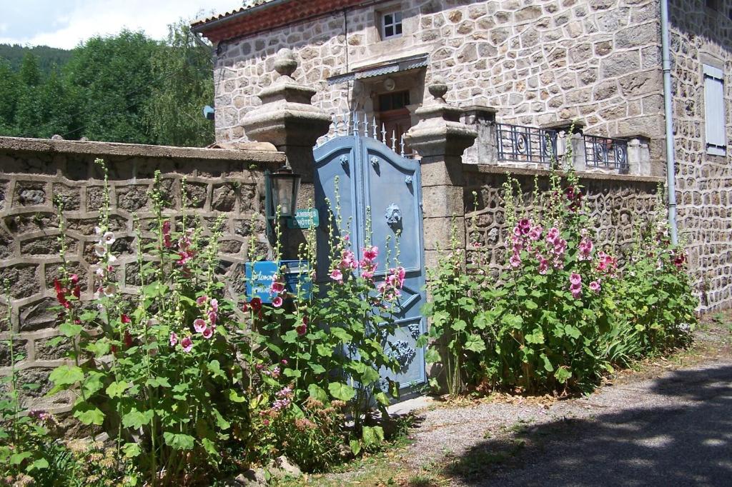 een stenen huis met een blauwe poort en bloemen bij Salomony Chambre d'Hôtes in Marcols-les-Eaux