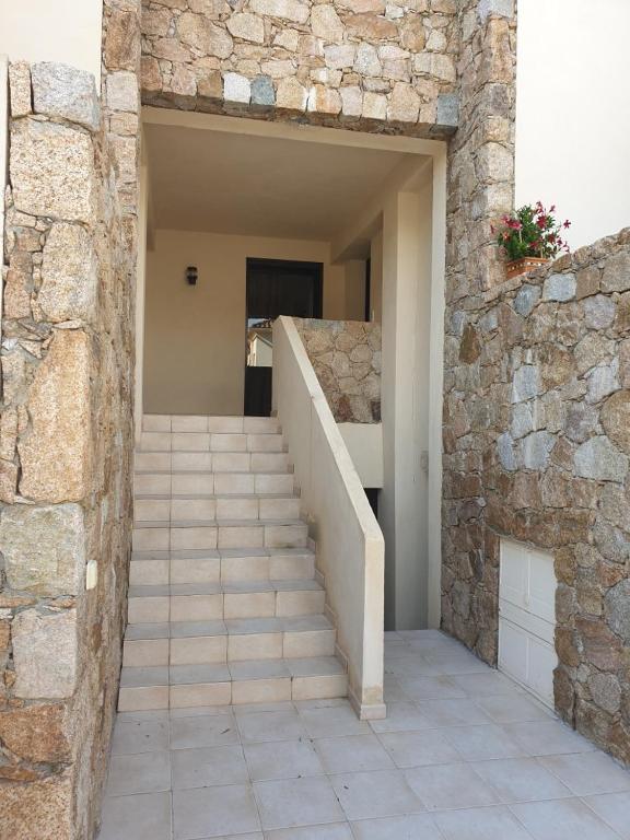 Un escalier mène à un bâtiment avec un mur en pierre. dans l'établissement Une chambre dans la résidence proche de plage, commerces et centre ville, à Calvi