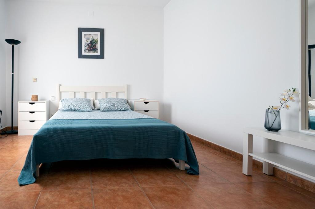 a white bedroom with a bed with a blue blanket at Casa Sagrario in Santa María de los Llanos