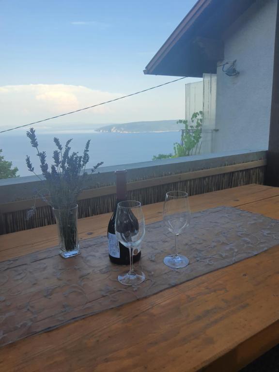 twee wijnglazen en een fles op een houten tafel bij Počitniška hiša Morski pogled in Mošćenička Draga