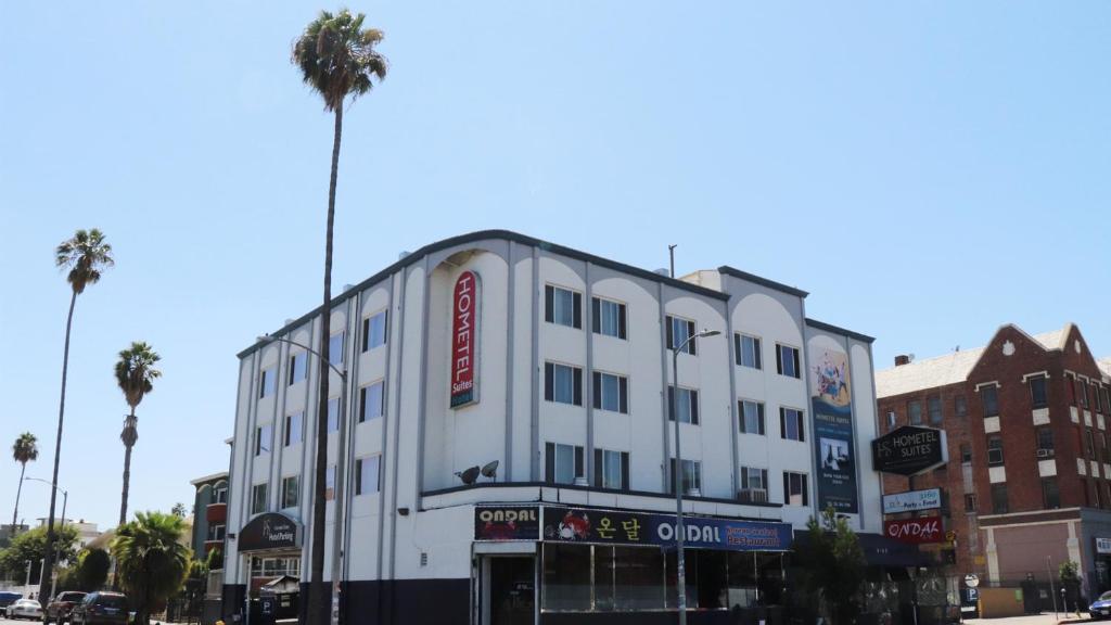 洛杉磯的住宿－Hometel Suites，一座白色的建筑,位于一条种有棕榈树的城市街道上
