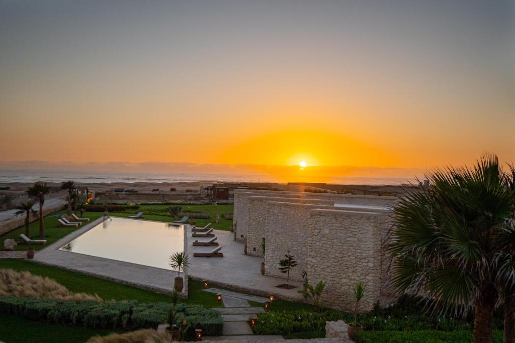 a sunset over a building with a swimming pool at BABERRIH Hôtel Hospitality Palaces & Resorts in Essaouira
