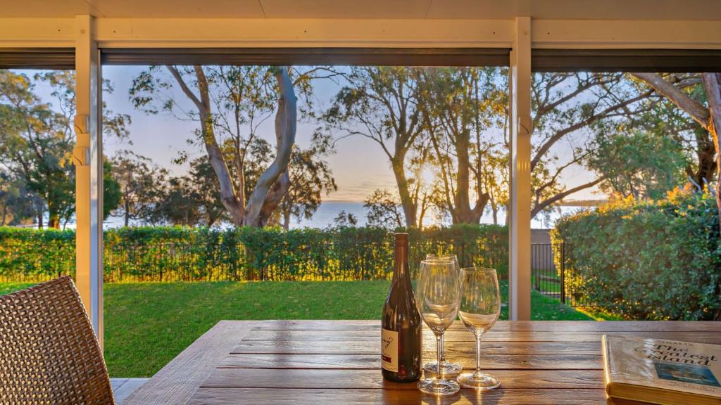 a bottle of wine and two glasses on a wooden table at Sunset Beach Luxury 24 in Soldiers Point