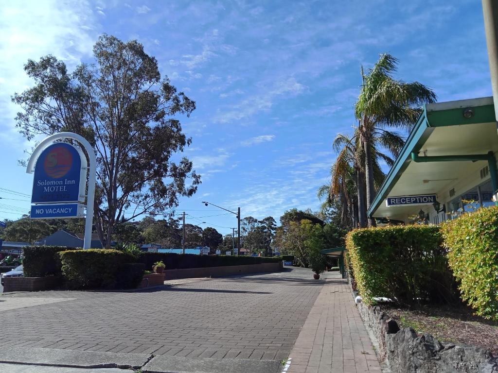 una calle con un edificio, un cartel y árboles en Solomon Inn Motel Figtree, en Wollongong