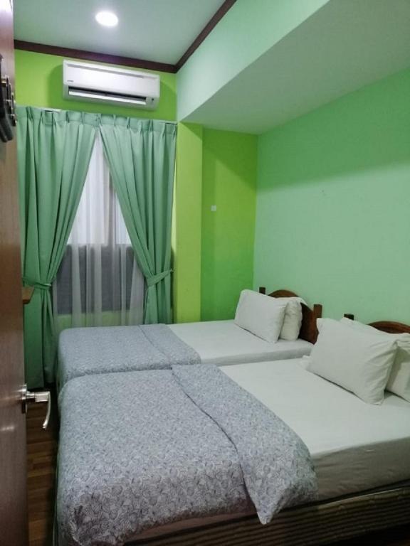 two beds in a room with green walls and a window at 1511 Guest House in Malacca