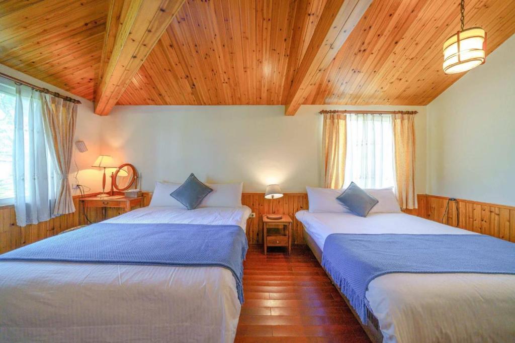 two beds in a room with wooden ceilings and windows at Fangshuh B&amp;B in Fenglin