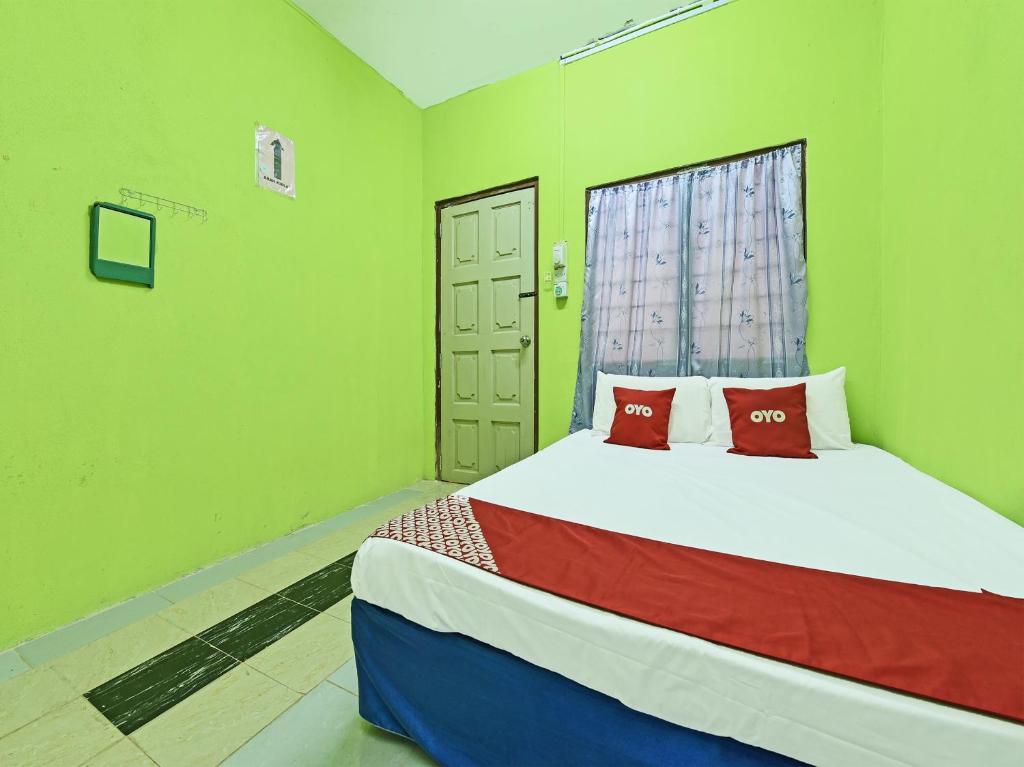 a bedroom with a bed with green walls and a window at OYO 90454 Haza Harmoni Guesthouse in Kota Bharu