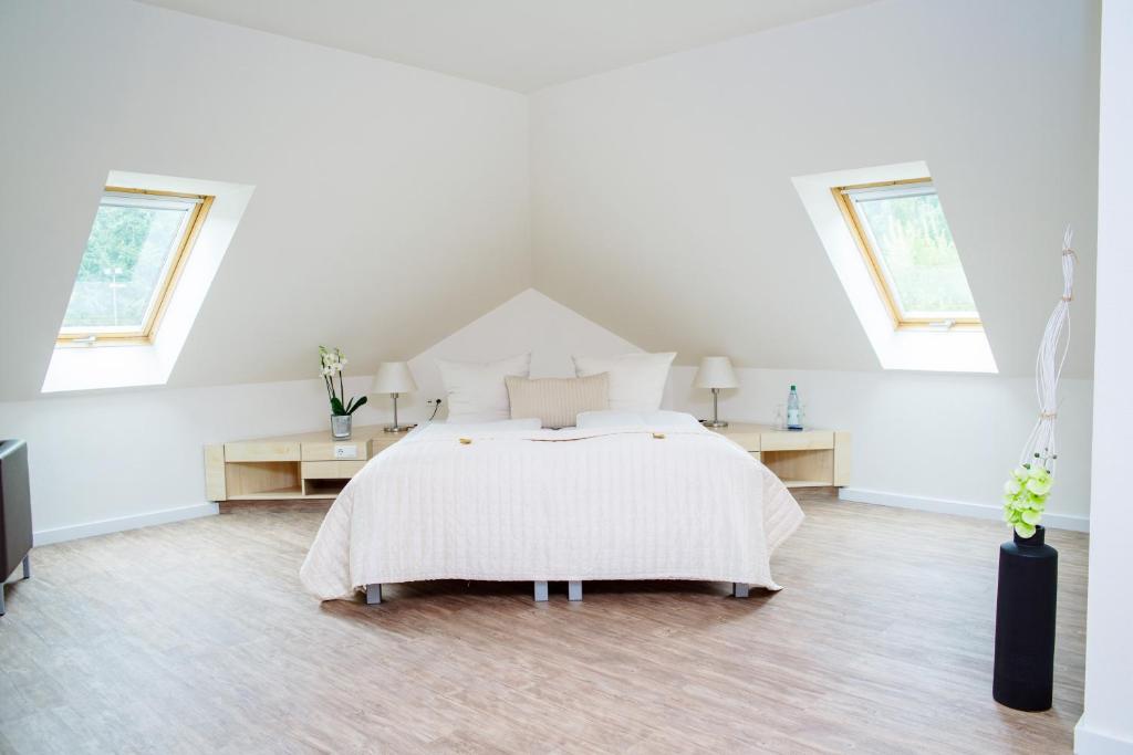a white bedroom with a bed and two windows at Sporthotel Fuchsbachtal in Barsinghausen