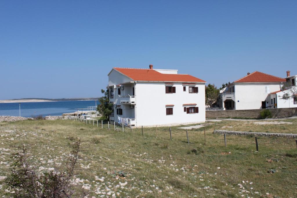 una casa blanca con techo rojo junto al agua en Apartments by the sea Kustici, Pag - 6353, en Zubovići