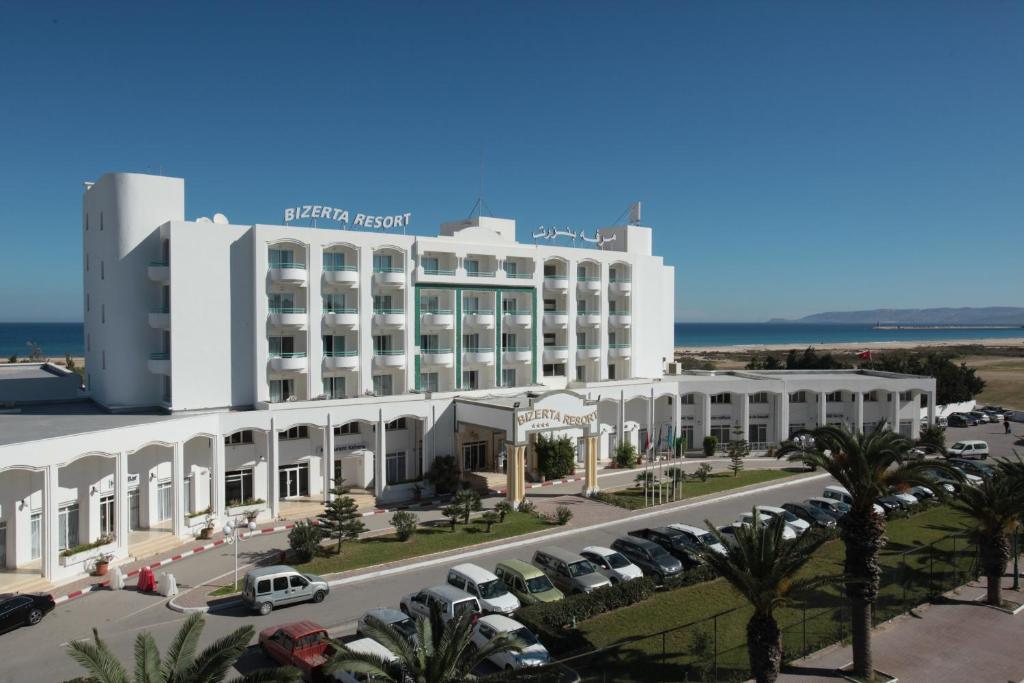 Un gran edificio blanco con coches aparcados en un estacionamiento. en Bizerta Resort Congres & SPA, en Bizerte
