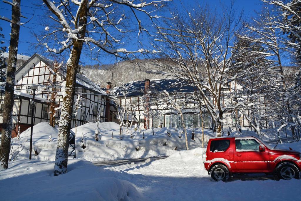 ein roter SUV in einem schneebedeckten Hof in der Unterkunft Hotel Sejour Mint in Hakuba in Hakuba