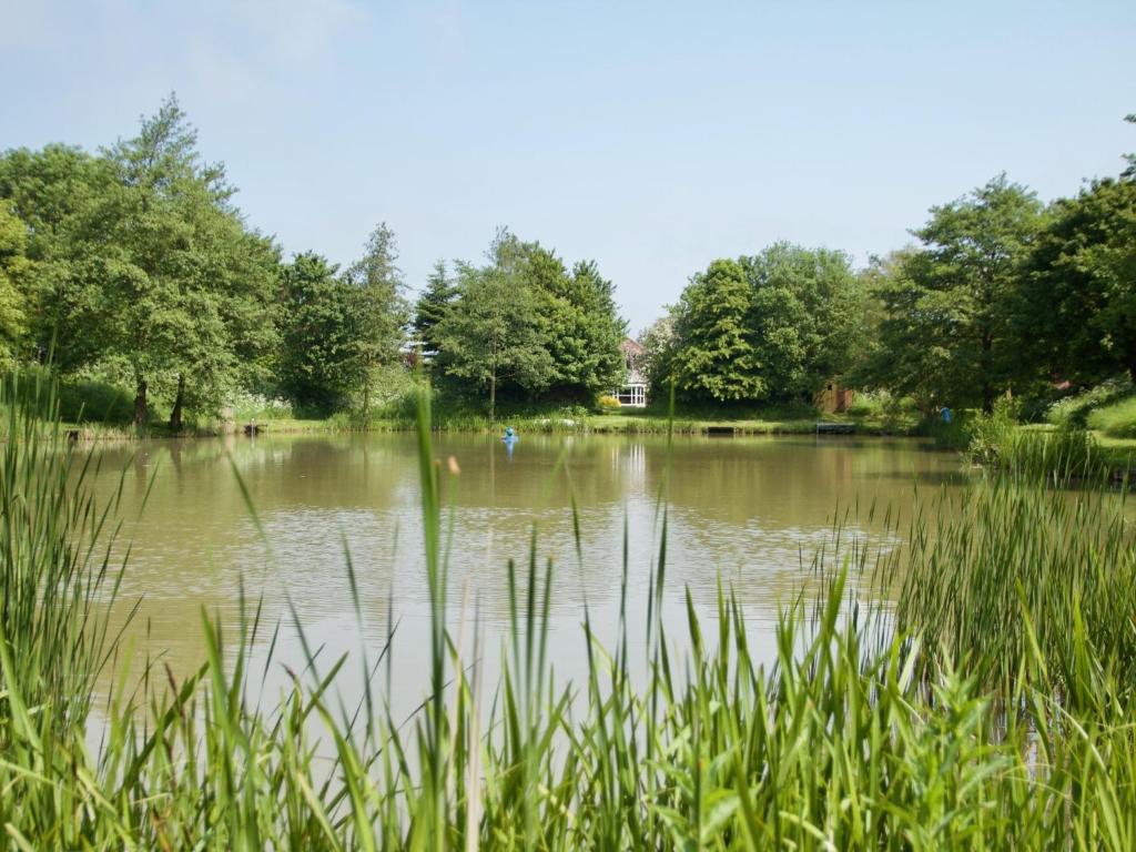 a large pond with trees and grass in a park at The Chestnuts Holiday Cottages in Burgh le Marsh