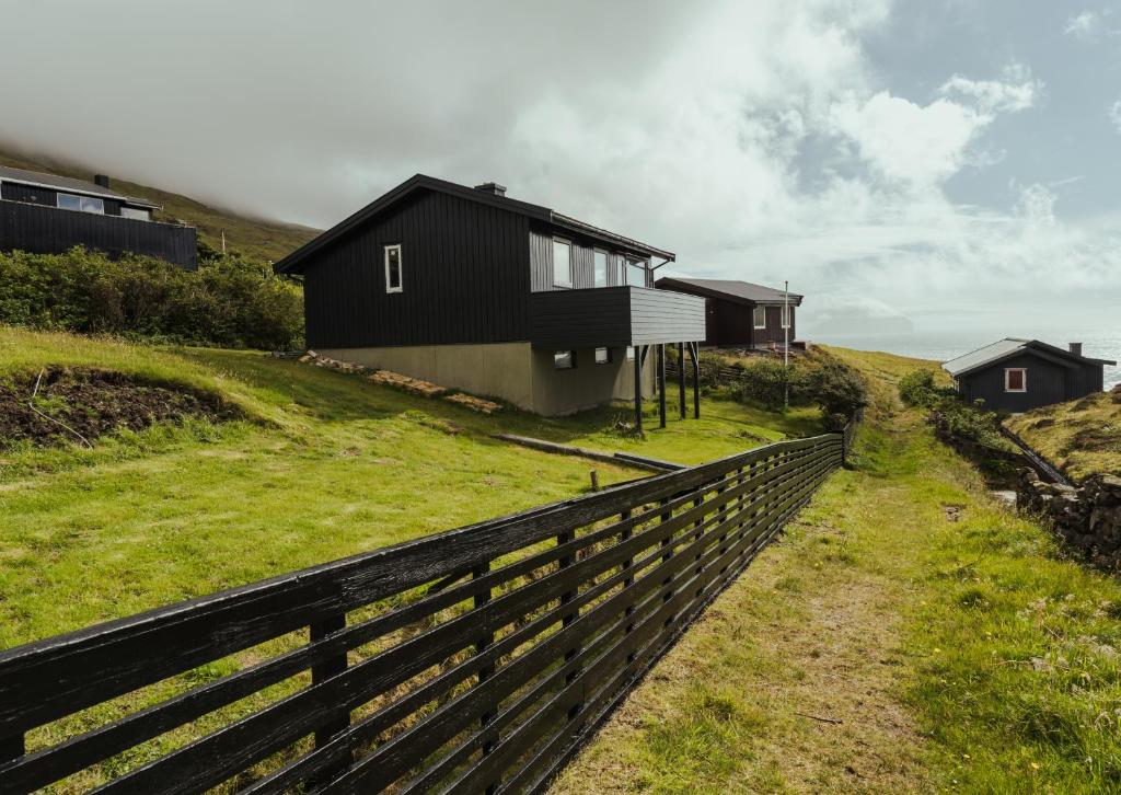 a black house on a hill with a fence at Cozy 2-bedroom house with a fantastic view in Leynar