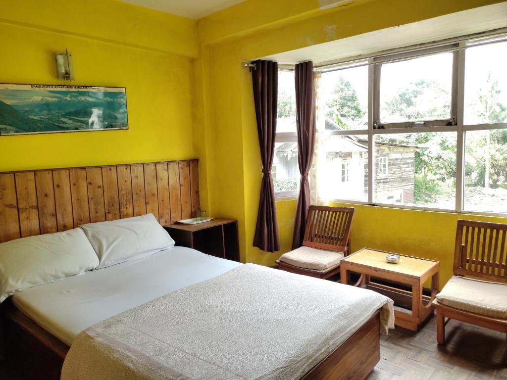 a bedroom with a bed and two chairs and a window at Hotel Mhelung in Darjeeling