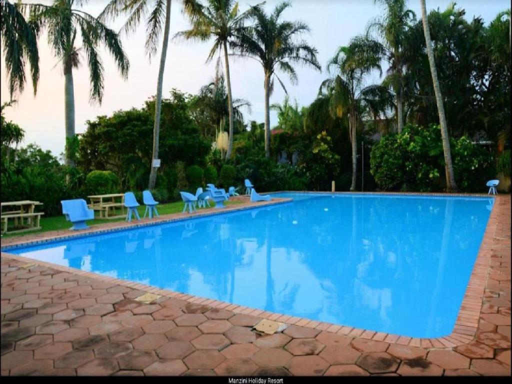 a large swimming pool with blue chairs and palm trees at Manzini Chalet No 34 in St Lucia