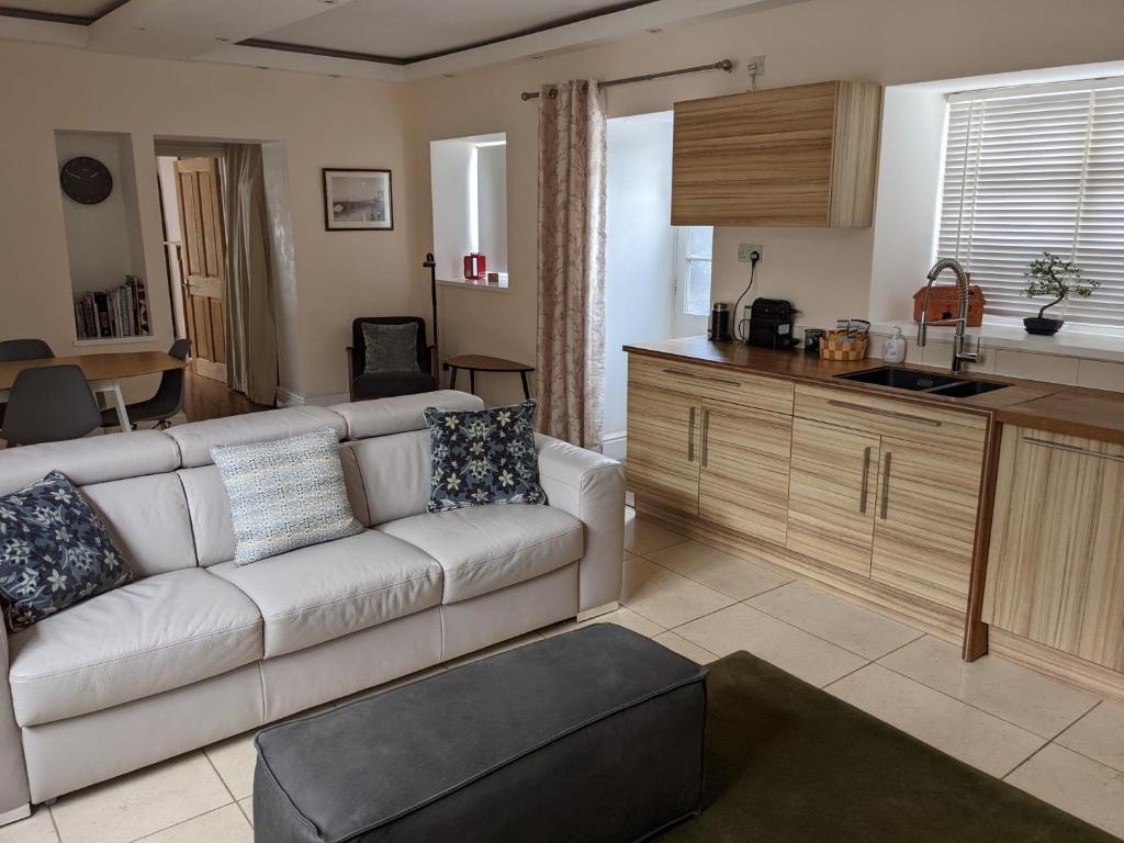 a living room with a white couch and a kitchen at The Lawns Spa Apartment in Holt