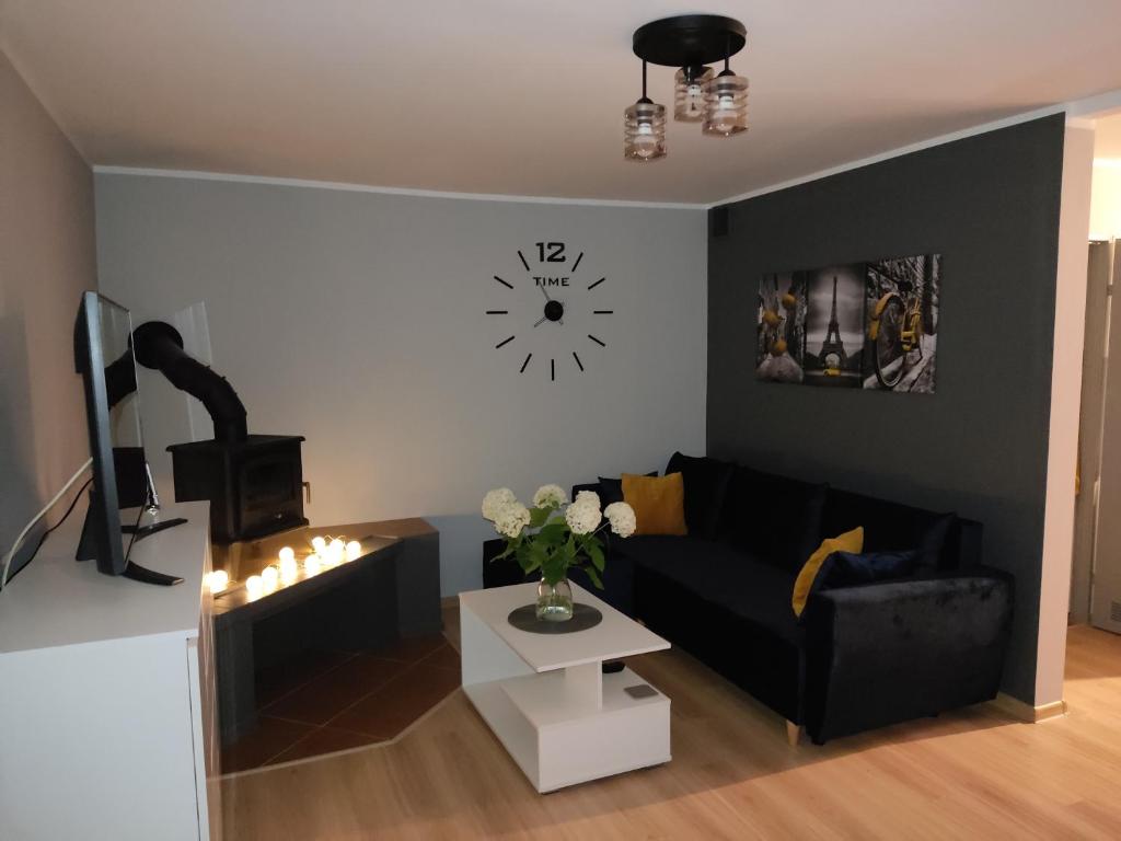 ein Wohnzimmer mit einem schwarzen Sofa und einer Uhr in der Unterkunft Domek z ogrodem in Mątki