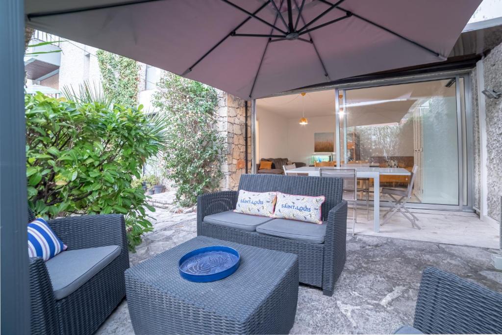 un patio con sillas, una sombrilla y una mesa en VILLA L'OASIS - à 80 m du bord de mer et plage en Cannes