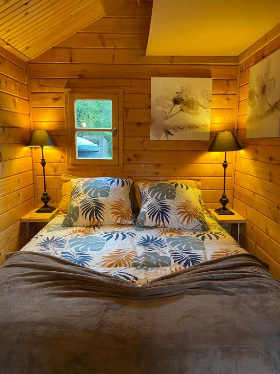 a bed in a wooden room with two lamps at Au chalet Fleuri in Ablon