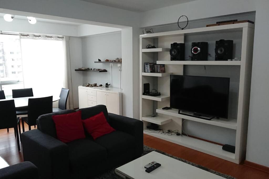 ein Wohnzimmer mit einem schwarzen Sofa und einem Flachbild-TV in der Unterkunft Elegante Flat en inmejorable ubicación - San Isidro in Lima