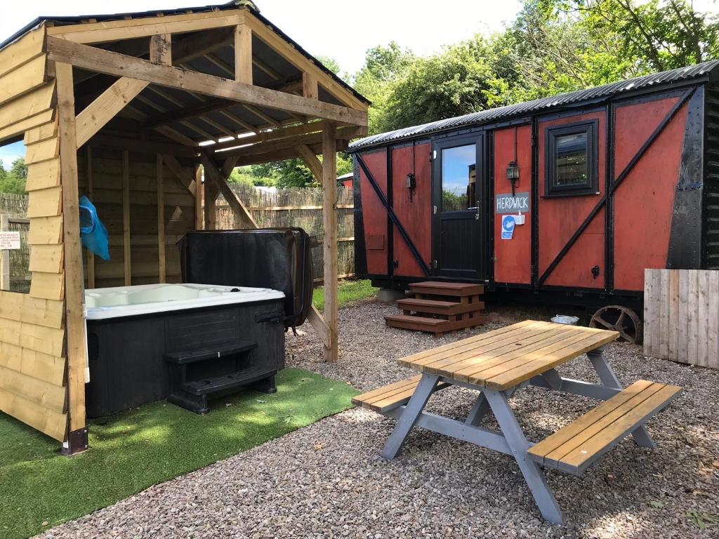 uma banheira de hidromassagem ao lado de um barracão e uma mesa de piquenique em Luxury cosy carriage with electric private hot tub em Hereford