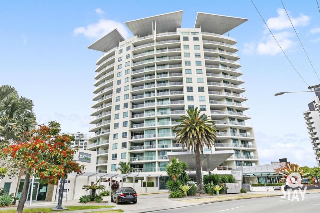 a tall white building with palm trees in front of it at Wings Apartments - QStay in Gold Coast