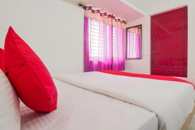 ein weißes Bett mit roten Kissen im Schlafzimmer in der Unterkunft Vangal Nest Peelamedu PSG stay in Coimbatore