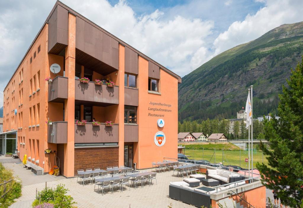 a building with tables and chairs in front of a mountain at Pontresina Youth Hostel in Pontresina